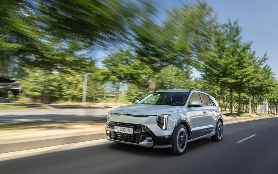 Kia Niro restylée blanche en mouvement sur une route bordée d’arbres